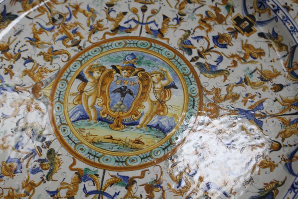 A 19th century Italian 17th century style maiolica charger, decorated with cherubs flanking a cartouche within bands of stylised beasts